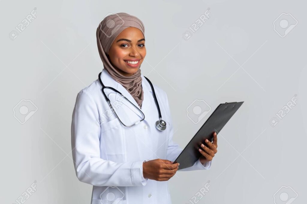 Smiling black muslim female doctor in hijab holding clipboard with clinical story of patient, posing over light background with free space
